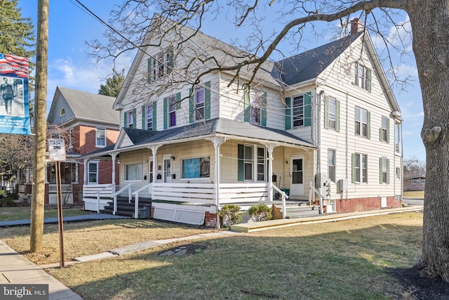 view of front facade with a chimney, a porch, and a front lawn