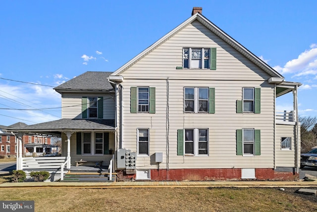 back of property featuring an attached carport, a shingled roof, covered porch, a lawn, and a chimney