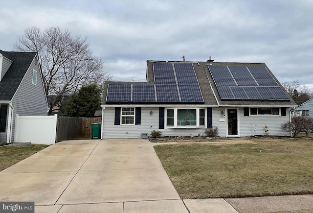 view of front of house with roof mounted solar panels, fence, and a front yard