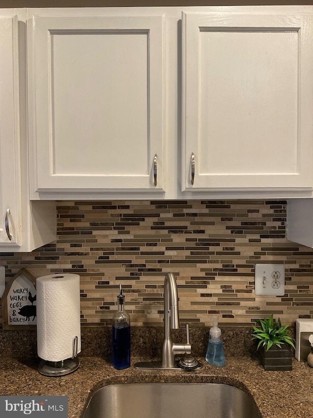 room details with tasteful backsplash, white cabinets, a sink, and dark stone countertops