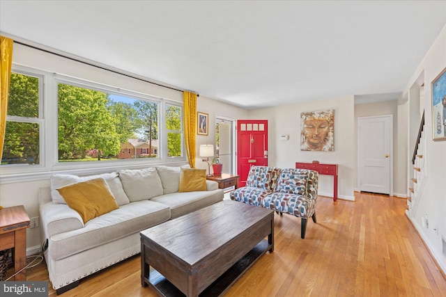 living room featuring baseboards, light wood-style flooring, and stairway