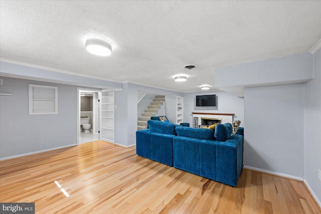 living room with a brick fireplace, a textured ceiling, built in features, wood finished floors, and stairway