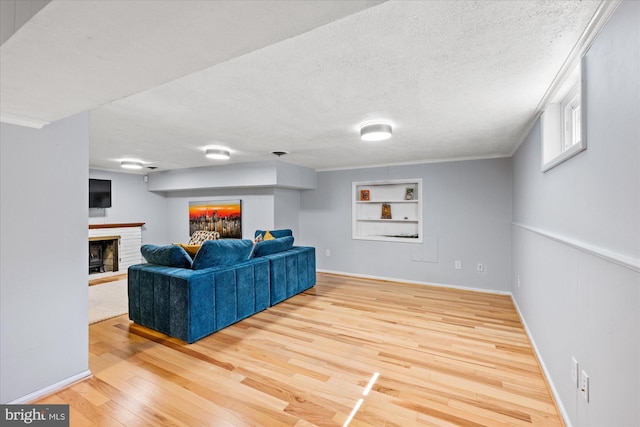 living room with a brick fireplace, a textured ceiling, built in features, wood finished floors, and ornamental molding