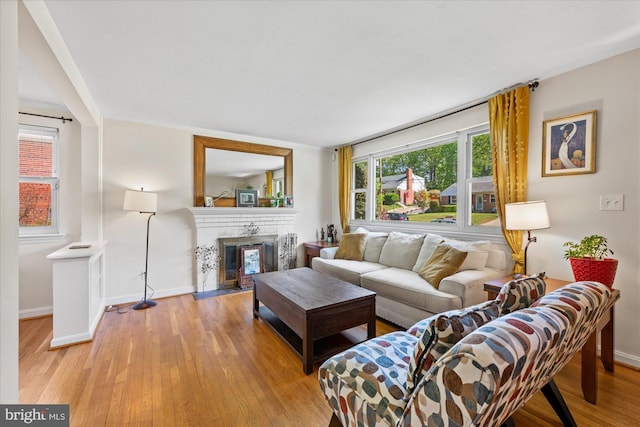 living area with baseboards, a brick fireplace, and light wood finished floors