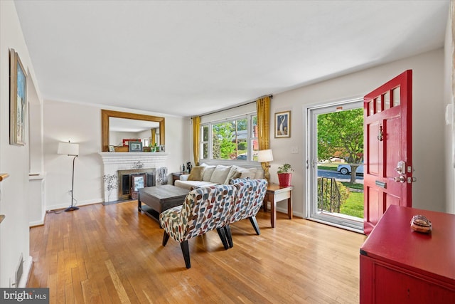 living room featuring a fireplace with flush hearth, baseboards, light wood finished floors, and visible vents