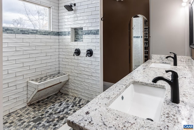 bathroom with a sink, a tile shower, and double vanity