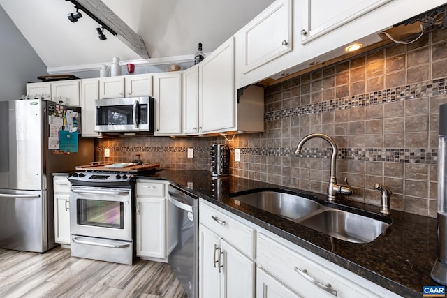 kitchen featuring tasteful backsplash, appliances with stainless steel finishes, dark stone countertops, white cabinetry, and a sink