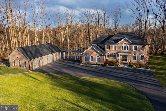 georgian-style home featuring a front yard, a view of trees, brick siding, and driveway