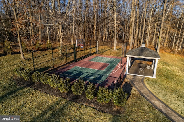 view of basketball court with basketball hoop, fence, and a lawn