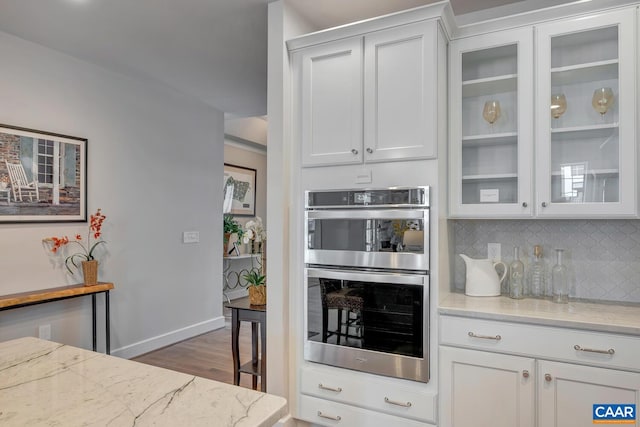 kitchen featuring stainless steel double oven, backsplash, glass insert cabinets, and white cabinets