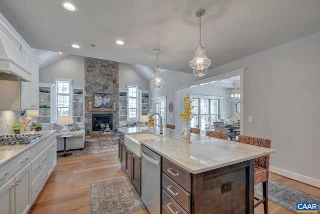 kitchen featuring white cabinets, a breakfast bar, stainless steel appliances, a stone fireplace, and a sink