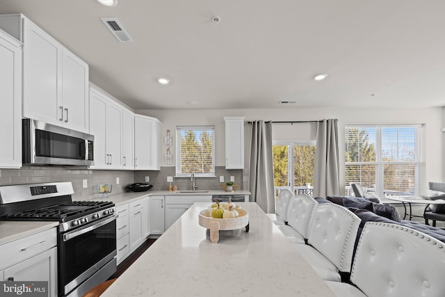 kitchen featuring a sink, open floor plan, appliances with stainless steel finishes, white cabinets, and decorative backsplash