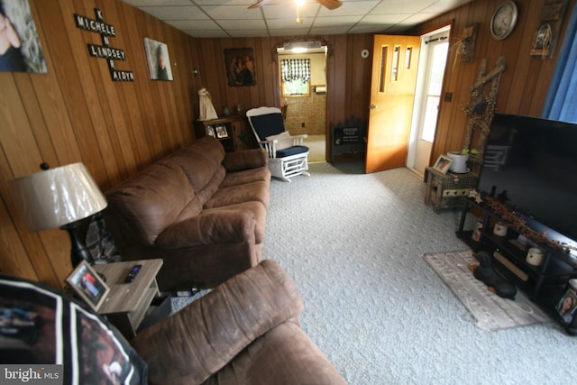 living room with a ceiling fan, a drop ceiling, wooden walls, and carpet flooring