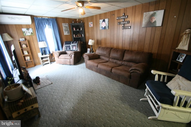 carpeted living room with ceiling fan, an AC wall unit, a drop ceiling, and wooden walls