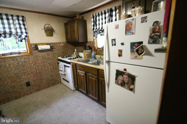 kitchen with white appliances, light colored carpet, brick wall, light countertops, and a sink