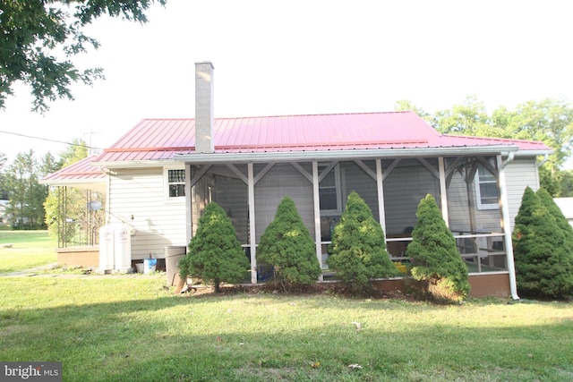 back of property with a sunroom, a chimney, metal roof, and a yard