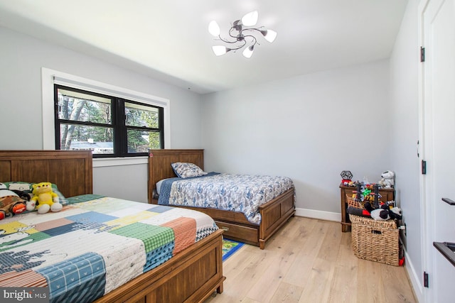 bedroom with a notable chandelier, light wood-style floors, and baseboards