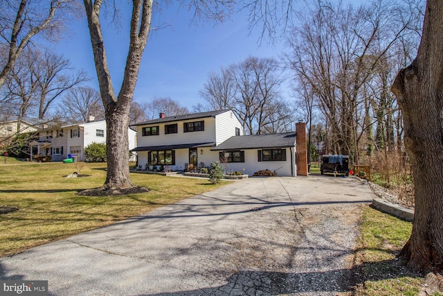 view of front of property featuring aphalt driveway, a chimney, and a front yard