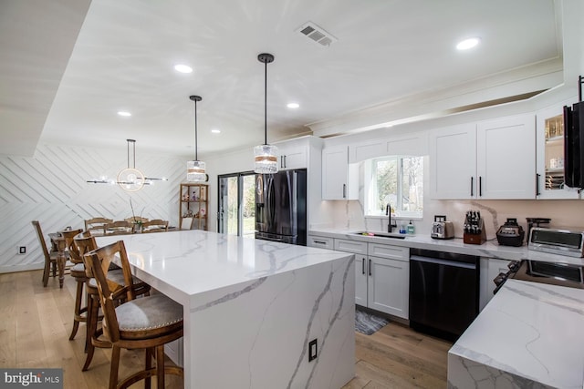 kitchen featuring visible vents, a kitchen island, a breakfast bar, a sink, and black appliances