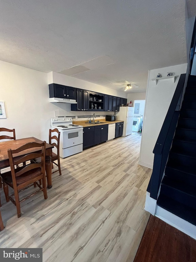 kitchen featuring white appliances, a textured ceiling, light wood-type flooring, under cabinet range hood, and a sink