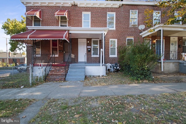 multi unit property featuring covered porch, brick siding, and fence