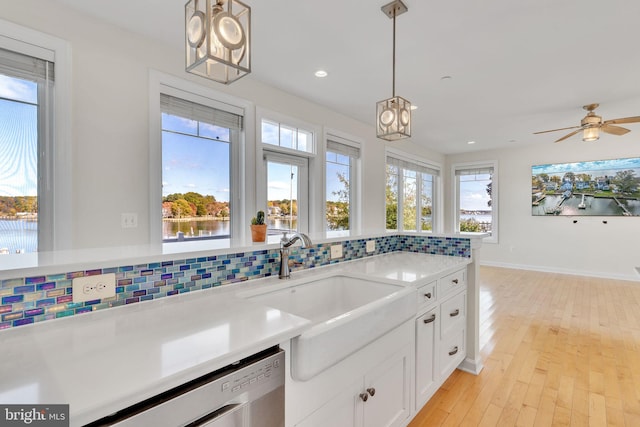 kitchen with a sink, white cabinetry, stainless steel dishwasher, backsplash, and pendant lighting