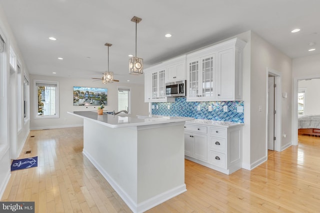 kitchen with light wood-style flooring, white cabinetry, light countertops, decorative backsplash, and stainless steel microwave