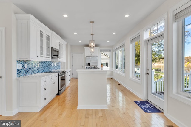 kitchen with decorative backsplash, white cabinets, stainless steel appliances, light countertops, and light wood-type flooring