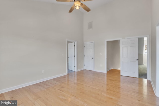 unfurnished bedroom featuring baseboards, visible vents, a ceiling fan, a towering ceiling, and light wood-type flooring