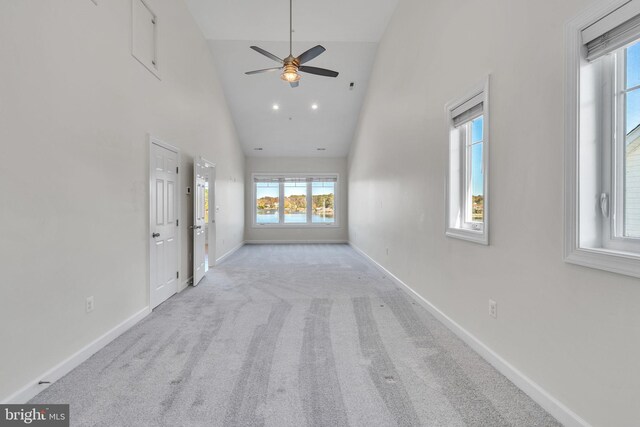 unfurnished living room with carpet floors, ceiling fan, high vaulted ceiling, and baseboards