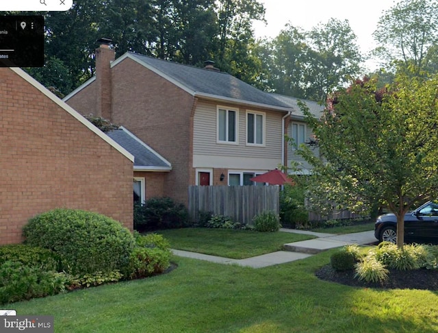 view of property exterior with brick siding, a lawn, a chimney, and fence