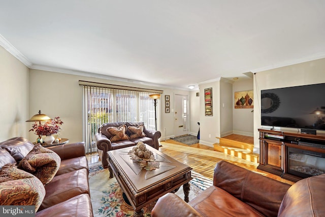 living room with ornamental molding, a glass covered fireplace, light wood-style flooring, and baseboards