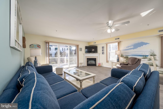 living area with ceiling fan, visible vents, wood finished floors, and a glass covered fireplace