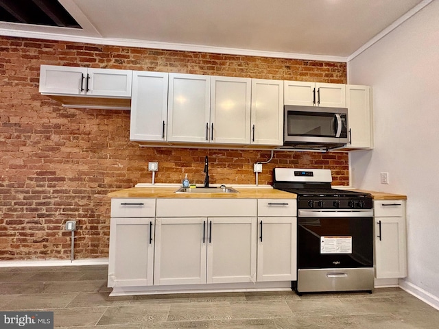 kitchen with brick wall, stainless steel appliances, a sink, white cabinetry, and baseboards