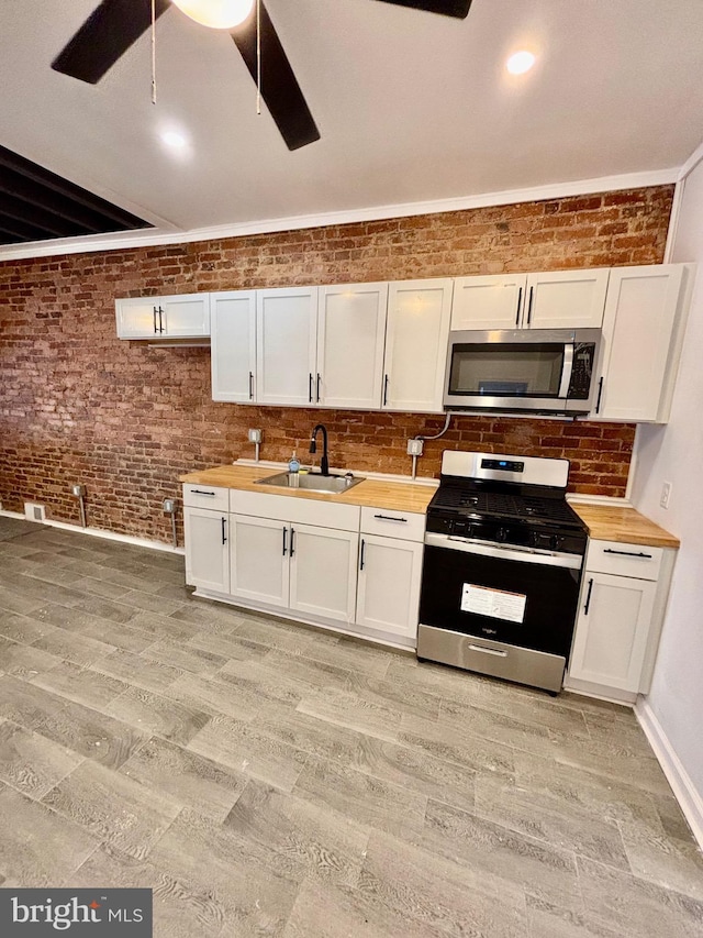 kitchen featuring white cabinets, a ceiling fan, brick wall, stainless steel appliances, and a sink