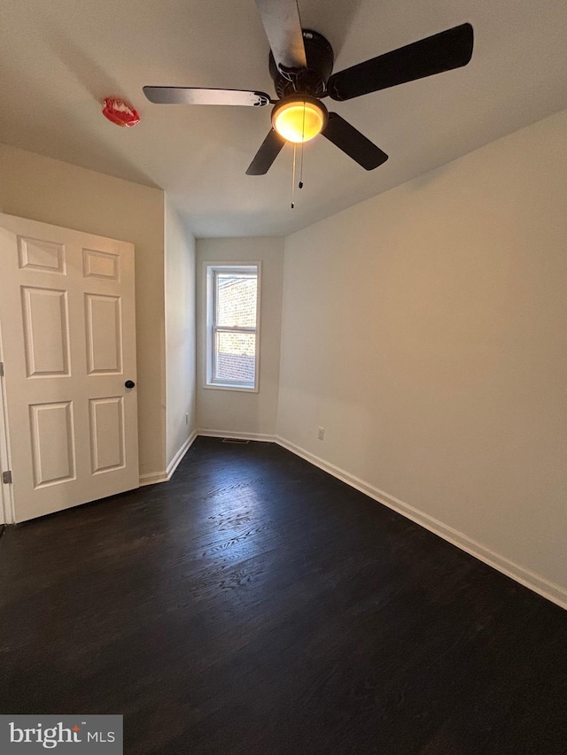 empty room featuring ceiling fan, dark wood-type flooring, and baseboards