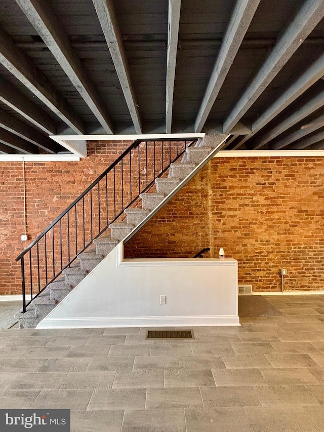 stairs with visible vents, brick wall, and beam ceiling