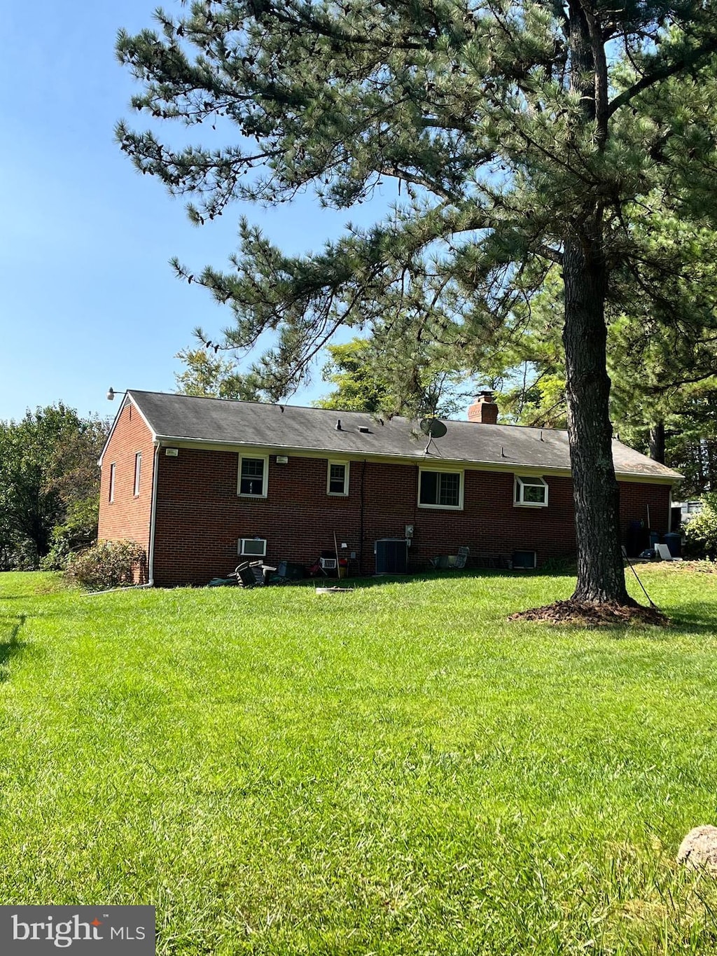 rear view of house featuring central AC unit, a lawn, and a chimney