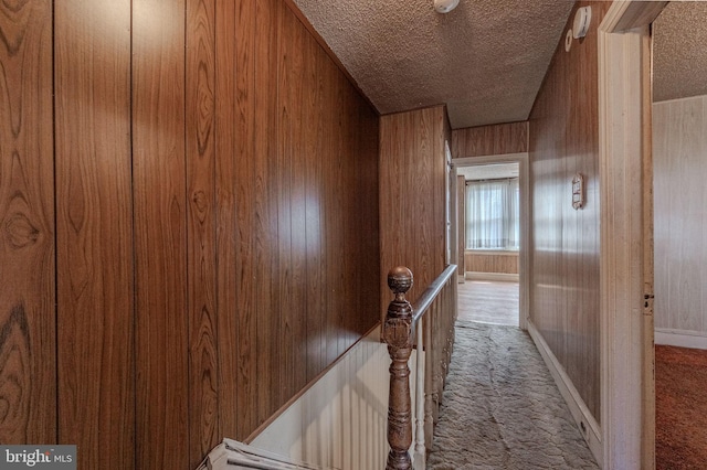 hallway with a textured ceiling, wood walls, carpet flooring, and an upstairs landing