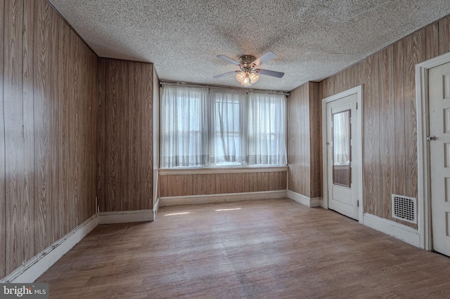 spare room featuring visible vents, wooden walls, a textured ceiling, and wood finished floors