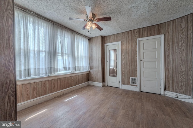 empty room featuring wooden walls, ceiling fan, a textured ceiling, and wood finished floors