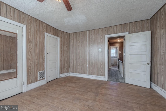 empty room with visible vents, wood walls, a textured ceiling, and wood finished floors