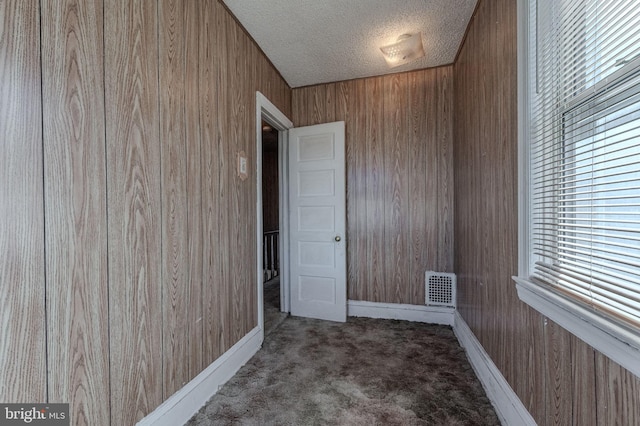 carpeted spare room with wood walls, baseboards, visible vents, and a textured ceiling