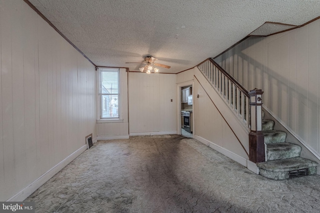 unfurnished living room featuring a textured ceiling, carpet flooring, visible vents, stairs, and ornamental molding