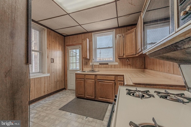 kitchen featuring a sink, light countertops, wood walls, light floors, and gas range gas stove