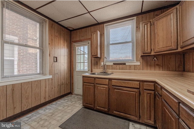 kitchen featuring brown cabinets, light floors, light countertops, a sink, and wood walls