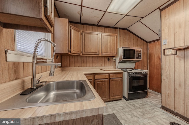 kitchen with range with gas stovetop, light floors, vaulted ceiling, a sink, and wooden walls