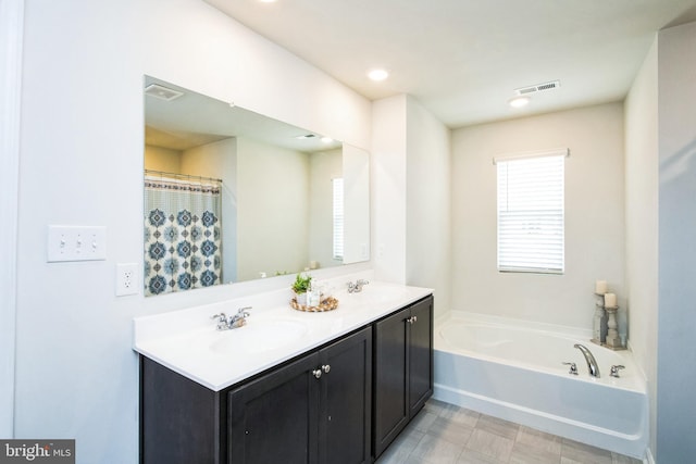 bathroom with a garden tub, double vanity, a sink, and visible vents