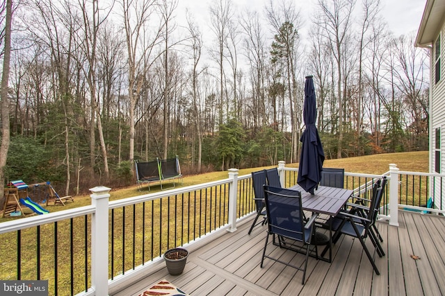 wooden deck with a trampoline, outdoor dining area, a playground, and a yard