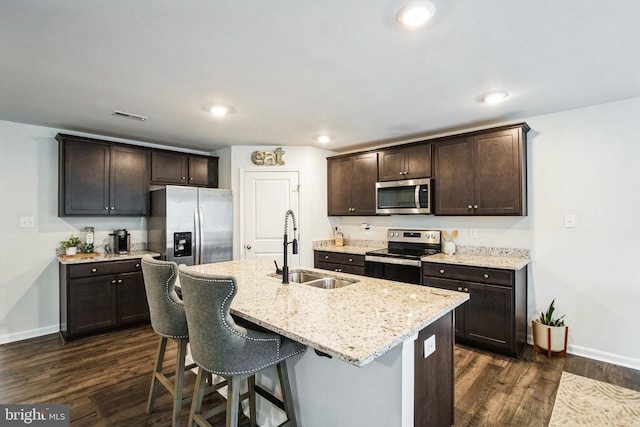 kitchen with appliances with stainless steel finishes, dark wood finished floors, a sink, and dark brown cabinets